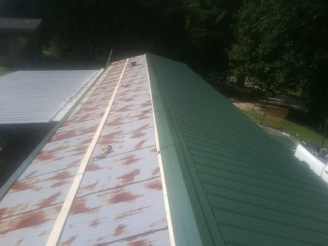 Old rusted panels beside newly installed green metal roofing — Wind Damage Roof Repair by Roofing Brothers in Hodges